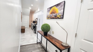 A hallway with a wooden bench, a potted plant, a floor lamp, and a painting on the wall. - Minutes to Churchill Downs- Pingpong table and Foosball (Louisville)