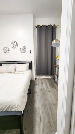 Un dormitorio con una cama, una mesita de noche con lámpara, una pared con adornos hexagonales y una cortina gris.