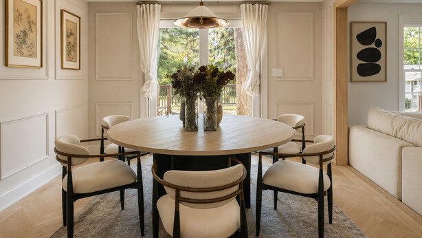 A dining area with a round table, six chairs, a vase with flowers, and a pendant light.