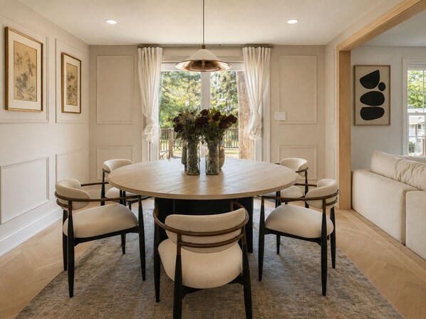 A dining area with a round table, six chairs, a vase with flowers, and a pendant light.