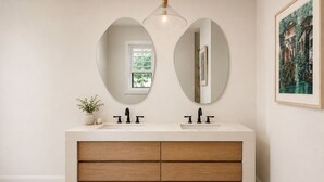A bathroom with a double sink vanity, wooden drawers, a hanging light fixture, and a framed painting on the wall.