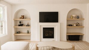 A living room with a fireplace, television, and shelves with decorative items.