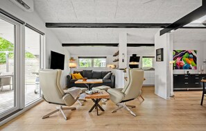 Ein modernes Wohnzimmer mit einer Couch, zwei Sesseln, einem Couchtisch und einem Fernseher.