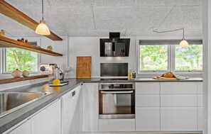 Eine moderne Küche mit Edelstahlgeräten, Holzregalen und großen Fenstern.