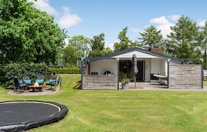 Ein kleines, eingeschossiges Gebäude mit überdachter Terrasse, Trampolin und Gartenmöbeln.