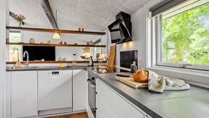 Et moderne køkken med hvide skabe, en Bosch opvaskemaskine, en træbordplade og et stort vindue med udsigt til grøn bevoksning.
