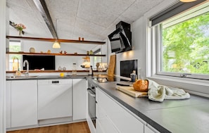 Eine moderne Küche mit weißen Schränken, einem Bosch Geschirrspüler, einer Holz Arbeitsplatte und einem großen Fenster mit Blick ins Grüne.