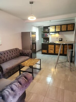 Ein Wohnzimmer mit einer Couch, einem Couchtisch, einer Küchenzeile mit Kühlschrank und einer Wendeltreppe.
