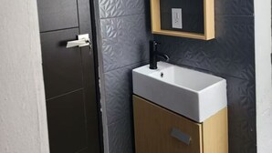 A bathroom with a white sink, a wooden cabinet, a mirror, and a door. - Apartment in El Chopo (Ciudad de México)