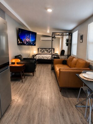 Ein kompaktes Hotelzimmer mit Bett, Sofa, Esstisch, Wand-Fernseher und einer Küchenzeile.
