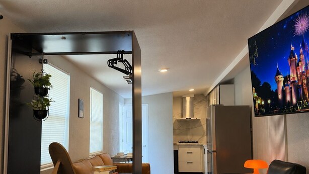 A modern interior with a bed, a seating area, a kitchen, and a TV displaying a castle. - The Ember Suite l Designer Guest House (Kissimmee)