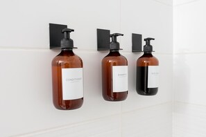 Three bottles of conditioner, shampoo, and body wash mounted on a white tiled wall. - Bright & Modern Toronto Escape | Near CN Tower & Rogers Centre (Toronto)