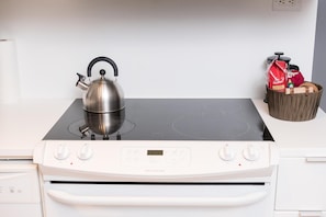 A kitchen with a stainless steel kettle on a black induction cooktop, a white refrigerator, and a basket with bags on the counter. - Bright & Modern Toronto Escape | Near CN Tower & Rogers Centre (Toronto)