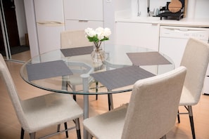 A round glass table with four chairs, a vase with white flowers, and a kitchen area in the background. - Bright & Modern Toronto Escape | Near CN Tower & Rogers Centre (Toronto)