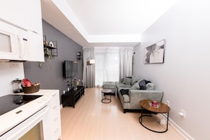 A modern living space with a kitchen, a grey sofa, a small table, and a TV. - Bright & Modern Toronto Escape | Near CN Tower & Rogers Centre (Toronto)