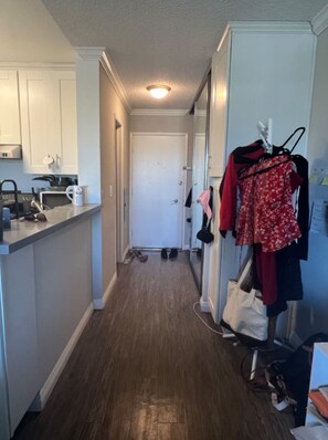 A narrow hallway with a kitchen area on one side, a door at the end, and a clothing rack with various items. - Top-Floor Studio. Pool, Hot Tub &FreeParking (Los Angeles)