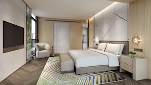 Quarto moderno com uma cama grande, uma poltrona, uma mesinha de cabeceira e televisão presa na parede.