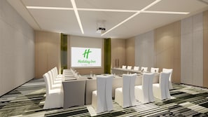 A conference room with a large screen displaying the Holiday Inn logo, white chairs, and a long table with water bottles. - Holiday Inn Yongkang (Jinhua)