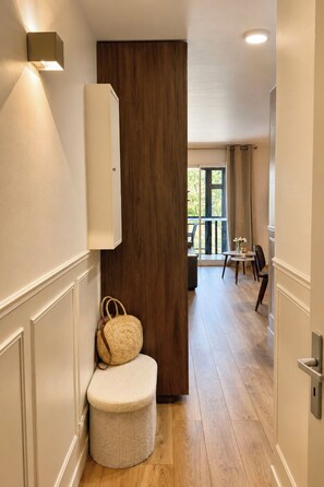 A hallway with a wooden door, a bench, a wall-mounted light, and a view into a dining area. - Résidence du golf by Interhome (Deauville-Trouville)