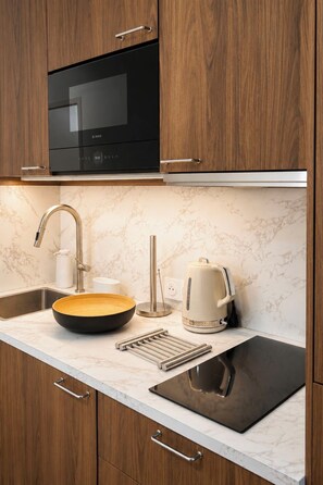 A kitchen with a black Bosch microwave, a stainless steel faucet, a white kettle, and a black sink. - Résidence du golf by Interhome (Deauville-Trouville)