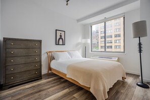 Un dormitorio con cama, cómoda, ventana con vistas y lámpara de pie.