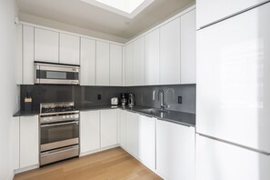 A modern kitchen with white cabinetry, stainless steel appliances, a black countertop, and a skylight above. - Blueground | Financial District, pool, nr Brooklyn Bridge (New York)