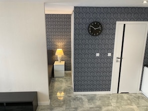 En gang med tapet, et ur, en dør og et natbord med en lampe.