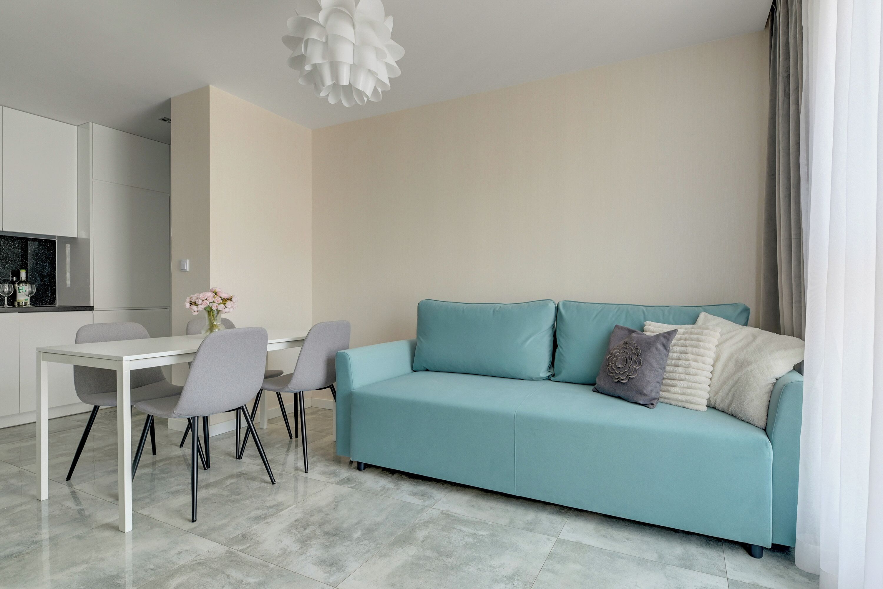 Una sala de estar moderna con un sofá azul claro, una mesa de comedor con sillas y una cocina al fondo.