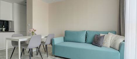 Una sala de estar moderna con un sofá azul claro, una mesa de comedor con sillas y una cocina al fondo.