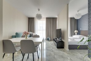 A hotel room with a dining table, chairs, a sofa, a TV, a bed, and a plant. - Angielska Grobla by Grand Apartments (Gdańsk)