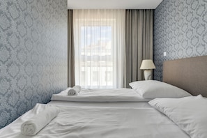 A hotel room with a neatly made bed, a lamp, and a window with curtains. - Angielska Grobla by Grand Apartments (Gdańsk)