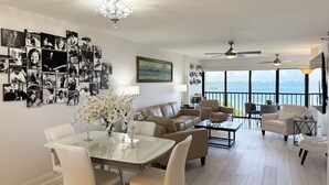 En rummelig opholdsstue med spisebord, sofaer og en balkon med havudsigt.