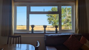 A room with a view through a window, a dining table, a sofa, and a radiator. - Grapnells Lodge Wallasea Island Rochford Essex (Rochford)