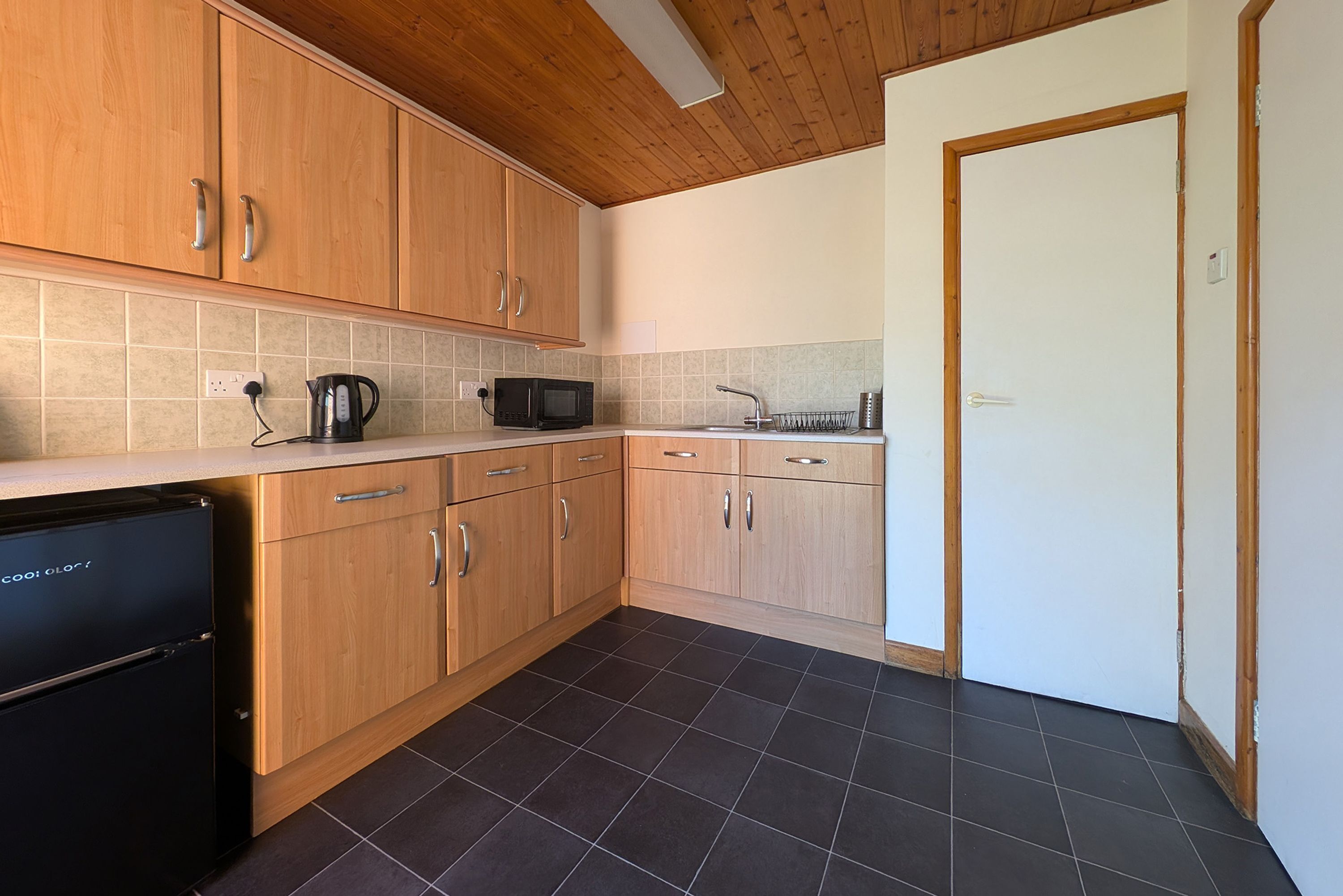 Eine Küche mit Holzausstattung, einem schwarzen Kühlschrank, einer Mikrowelle und einem Wasserkocher.