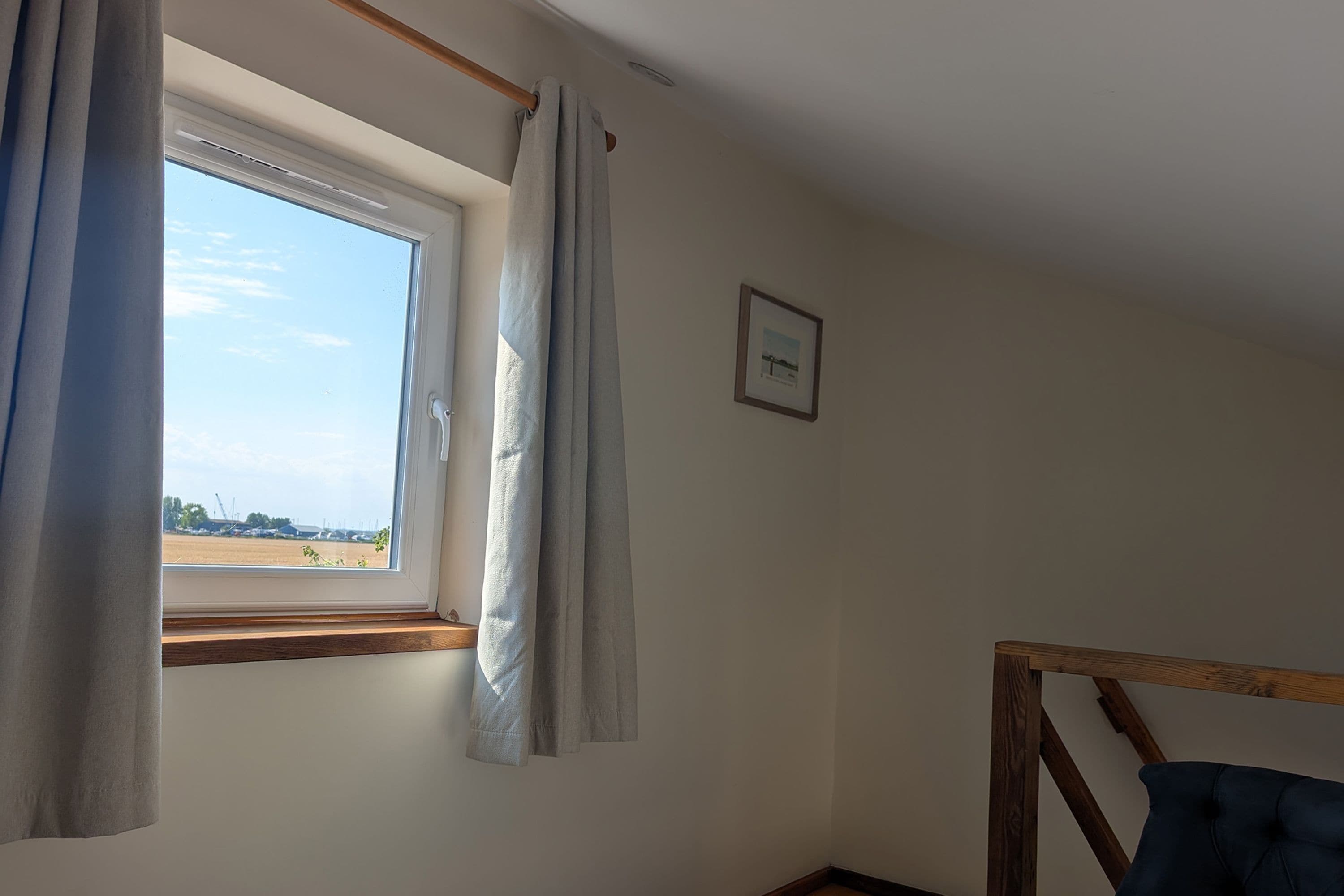 A room with a window, a wooden headboard, and a framed picture on the wall.