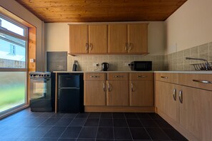 A modern kitchen with wooden cabinets, a black refrigerator, a stove, and a microwave. - Grapnells Lodge Wallasea Island Rochford Essex (Rochford)