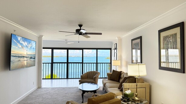 A spacious living room with a large window overlooking a body of water, a ceiling fan, and a view of the sea. - Sandpiper Key Waterfront Views & Pool (Englewood)
