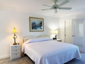 Ein Schlafzimmer mit Bett, Nachttischen, Deckenventilator, gerahmtem Gemälde und einer Tür.