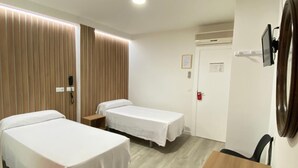 A hotel room with two beds, a wooden table, a desk, a mirror, and a door with a fire alarm.