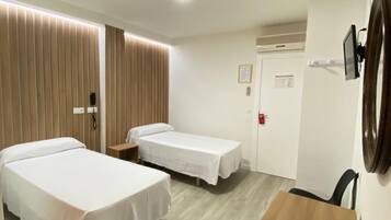 Ein Hotelzimmer mit zwei Betten, einem Holztisch, einem Schreibtisch, einem Spiegel und einer Tür mit Rauchmelder.