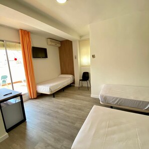 A hotel room with two single beds, a desk with a chair, a TV, and an air conditioning unit. - Hotel Victoria Centro (Almunecar)