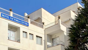 A multi-story hotel with balconies, a red sign for a restaurant, and outdoor seating.