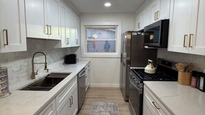 A modern kitchen with white cabinets, stainless steel appliances, and a window. - Modern Backyard Paradise Pool & Spa Near Dallas (Farmers Branch)