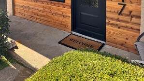 A building with a wooden facade, a black door, and a welcome mat. - Modern Backyard Paradise Pool & Spa Near Dallas (Farmers Branch)