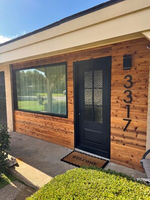 A building with a wooden facade, a black door, and a welcome mat. - Modern Backyard Paradise Pool & Spa Near Dallas (Farmers Branch)