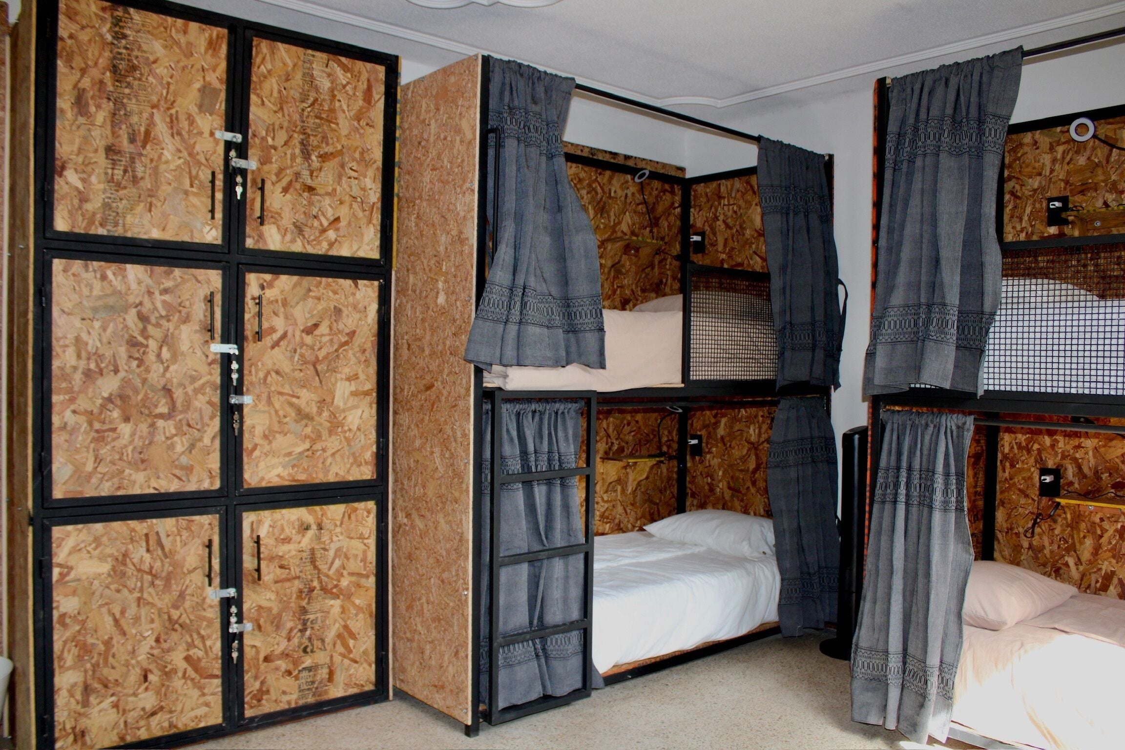 A bunk bed room with a wooden wall panel design, a single bed with a white mattress, and grey curtains.