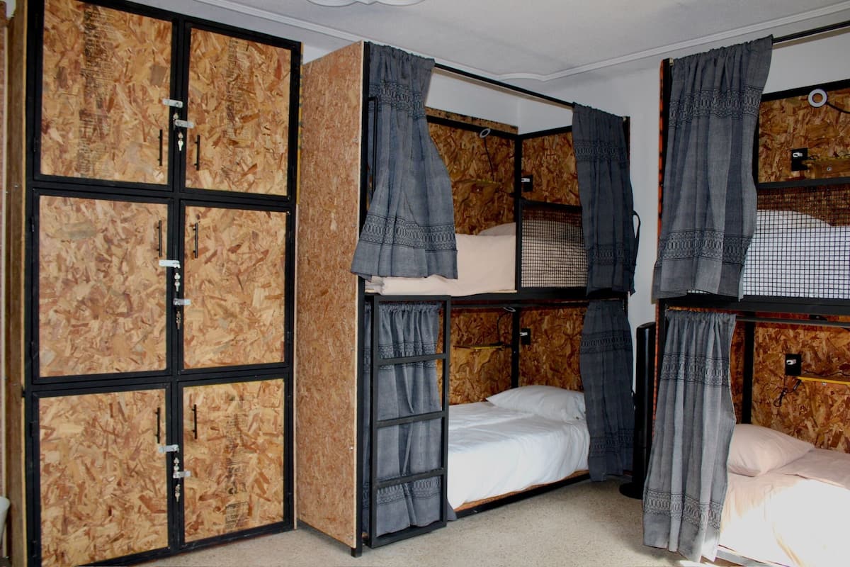 Habitación con literas, panel de pared de madera, una cama individual con colchón blanco y cortinas grises.