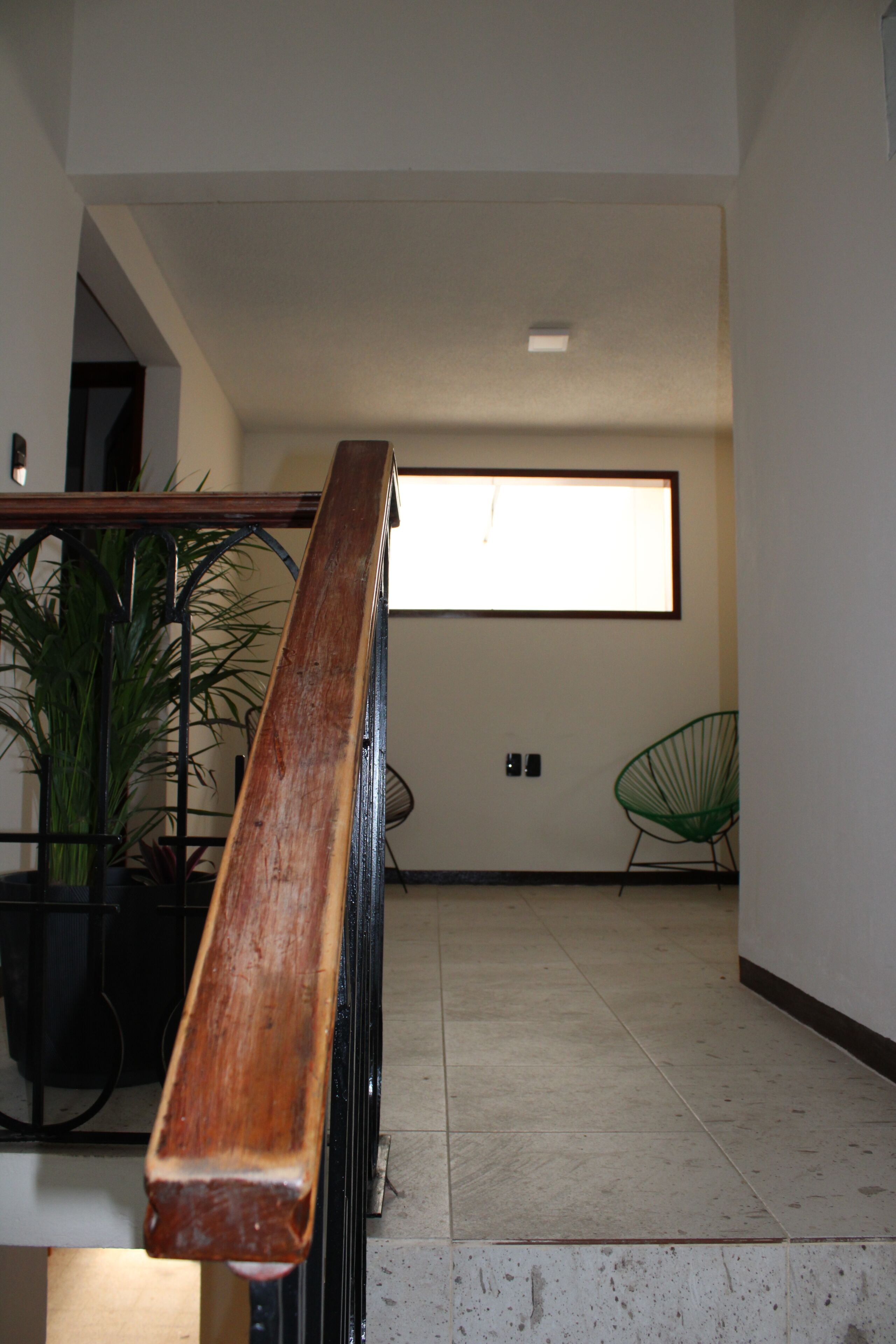 Eine Treppe mit Holzhandlauf, einem Blumentopf, einem grünen Stuhl und einem Fenster mit Tageslicht.