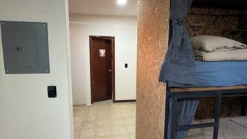 Une pièce avec un lit superposé, une porte avec un panneau indiquant la sortie, un luminaire fixé au mur et une poubelle.