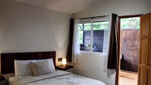 A bedroom with a bed, a bedside table with a lamp, a window with curtains, and a wooden door. - Luffa Hostel (Oaxaca)